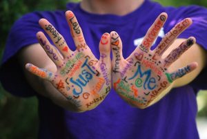 a person extends their palms in front of them. the hands have different descriptors written on them, including "Just Me"