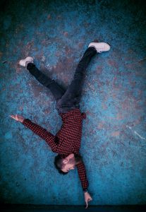 a man does a handstand using only his index finger, against a mottled blue wall