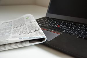 a folded newspaper partially covers the keyboard of an open laptop computer