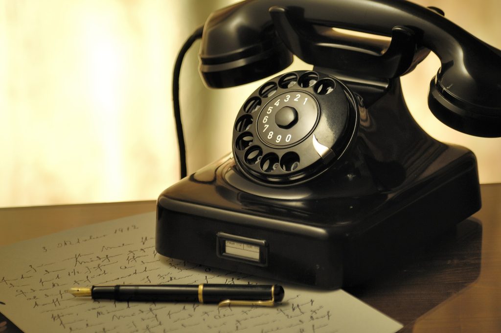 a rotary dial desktop phone sits atop a page of handwritten notes