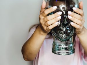 a woman holds a glass mold of a human head in front of her face