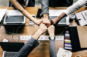 Five arms extend into a team fist bump over a collaborative workspace