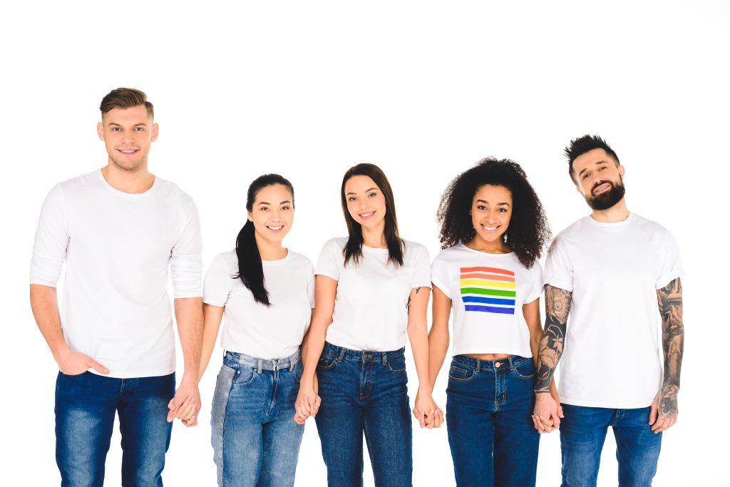 five young people of multiple ethnicities, holding hands. one is wearing a t-shirt with a rainbow flag on it