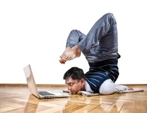 Indian businessman doing yoga and looking at laptop in the office at white background. Free space for your text