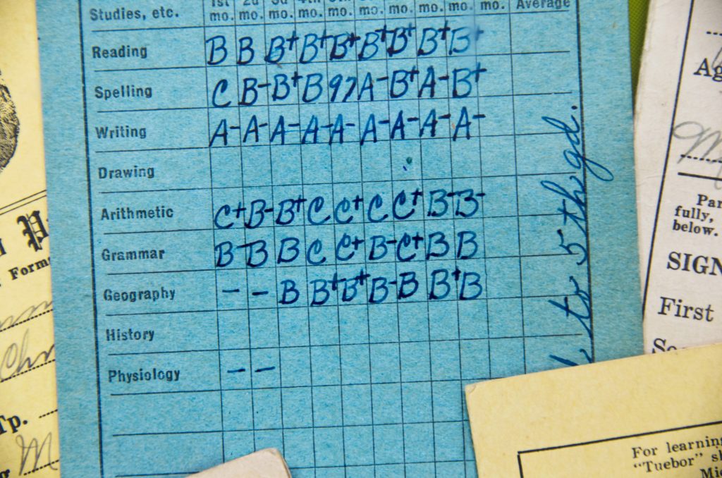 Picture of a traditional, hand-written school report card, showing grades for elementary school subjects such as Writing and Arithmetic.