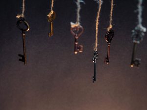 A lot of different old keys from different locks, hanging from the top on strings. Finding the right key, encryption, concept. Retro vintage brass keys on a dark background, low depth of field